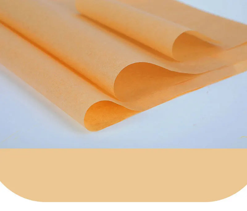 A stack of orange non-stick baking sheets rolled up on a white surface.