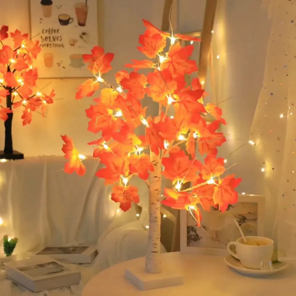 An LED maple leaf table lamp with warm glow illuminates autumn leaves on a white surface.
