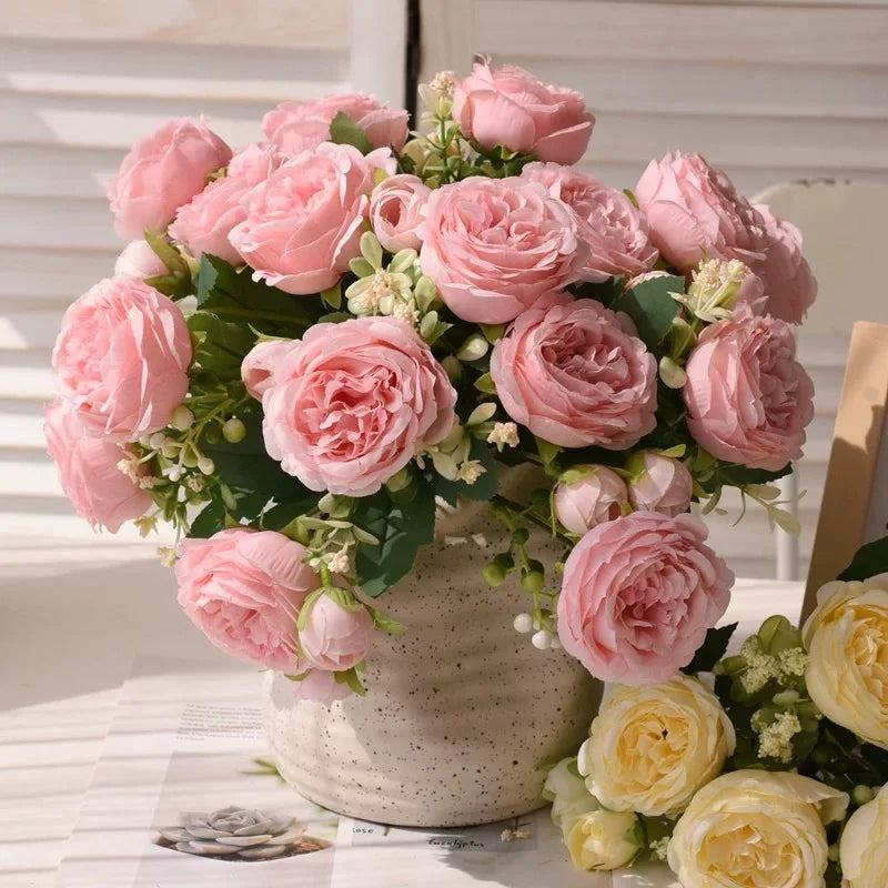 A bouquet of pink silk peony roses in various shades arranged in a ceramic vase.