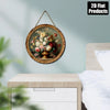 A round vintage floral wall art piece featuring roses and greenery, framed in gold wood, hanging on a light green wall.
