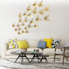 A set of 3D hollow butterfly wall decals in gold and white fluttering on a white wall above a modern sofa.