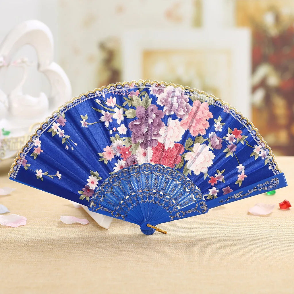 A blue hand fan decorated with pink and purple floral embroidery resting on a light-colored surface.