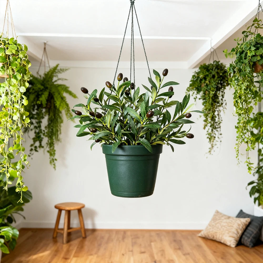 An artificial olive tree branch with green leaves and dark berries hanging from a pot in a bright room.
