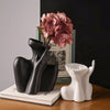 A black ceramic figural vase shaped like an artistic human form sits next to a white candle holder on a wooden surface.