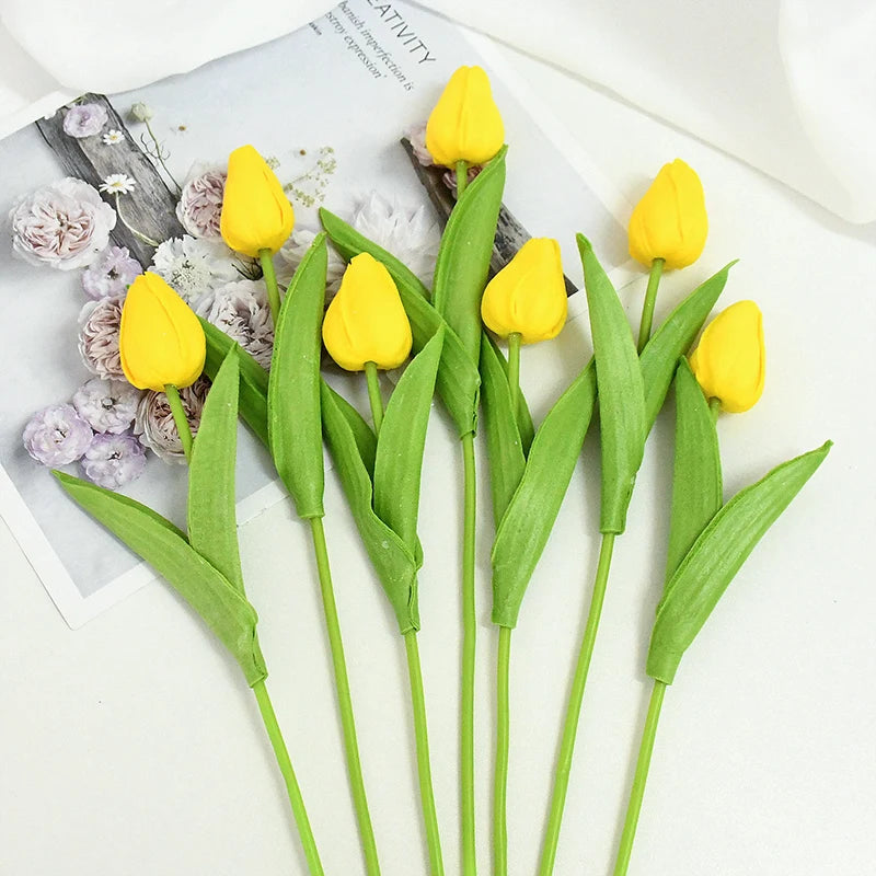 A bouquet of yellow artificial tulips with green stems and leaves displayed on a white background.