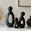 A set of three black resin figures depicting a family silhouette on a white marble surface.