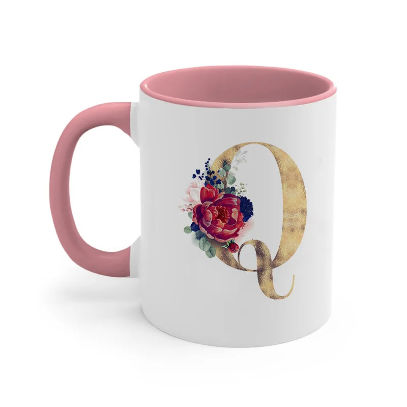 A pink ceramic coffee mug with a gold letter Q initial decorated with floral accents.