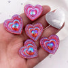 A hand holds a set of twelve heart-shaped pink and iridescent resin rhinestone flatbacks.