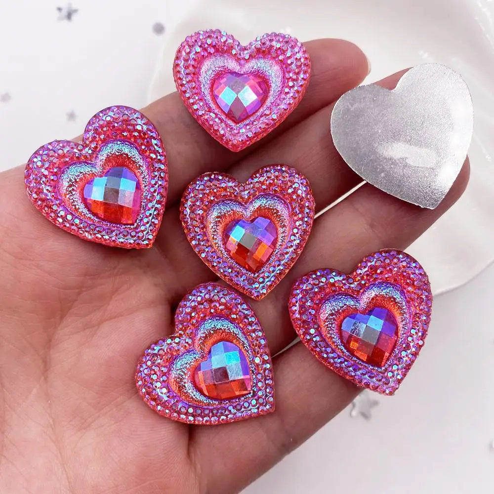 A hand holds a set of twelve heart-shaped pink and iridescent resin rhinestone flatbacks.