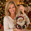 A smiling woman holds a finished Christmas pearl diamond painting suncatcher with a metal chain.