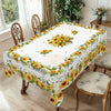 A white tablecloth with a yellow and green sunflower print set on a wooden dining table.