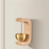 A wooden doorbell with a copper bowl hangs on a wall, featuring a curved wooden frame and a hanging bell.