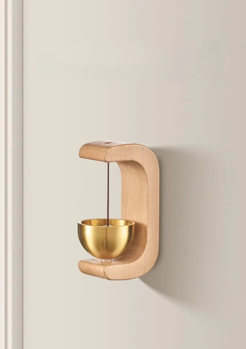 A wooden doorbell with a copper bowl hangs on a wall, featuring a curved wooden frame and a hanging bell.