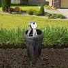 A silver key hider with a handle is placed in a dark pot in a grassy garden area.