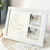 A white photo frame displaying three paw prints, featuring a cat's face in each print.
