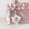 A pink satin pouch holds a clear photo album keychain with a heart design.