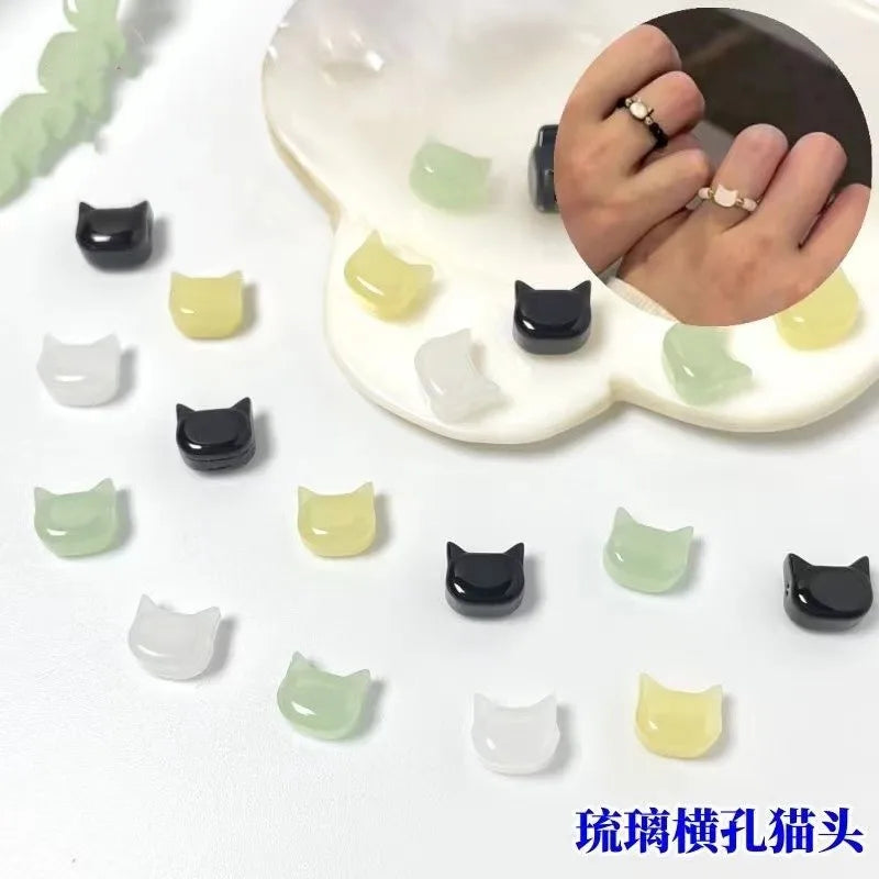 A collection of black and light green cat head glass beads for jewelry making, shown next to a hand for scale.