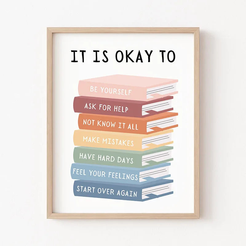 A framed print with the text It Is Okay To followed by a stack of colorful books encouraging self-acceptance and resilience.