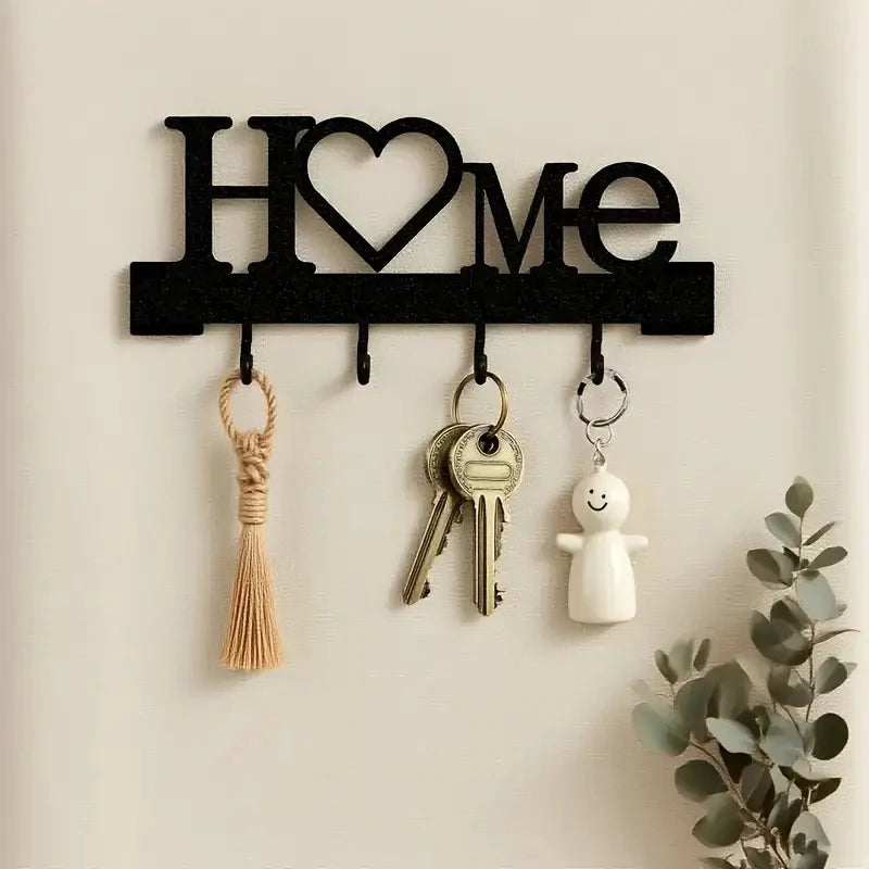 Black letter H O M E wall key holder with four hooks mounted on a beige wall.