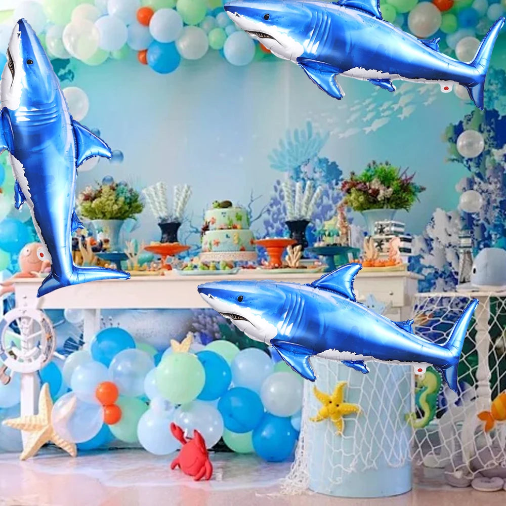 Blue and silver shark foil balloons decorating an ocean-themed party backdrop with sea life elements.