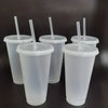 A collection of clear reusable tumblers with lids and straws standing upright on a dark surface.