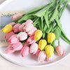 A bouquet of artificial pink and yellow tulips with green stems displayed on a white plate.