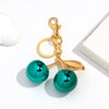 Gold-toned pendant keychain featuring a bright teal resin cherry charm.
