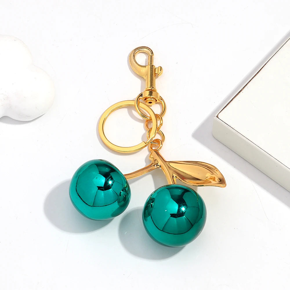 Gold-toned pendant keychain featuring a bright teal resin cherry charm.