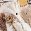 Bouquet de queues de lapin de pampas séchées arrangé sur un tissu en lin blanc avec des éléments naturels et des ciseaux