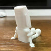A white 3D printed Moai statue figurine with movable joints standing on a wooden surface.