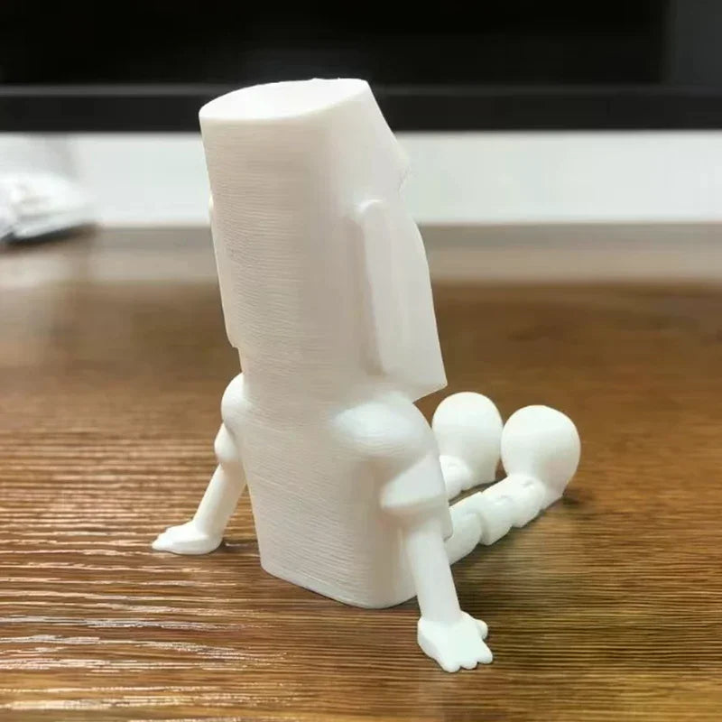 A white 3D printed Moai statue figurine with movable joints standing on a wooden surface.