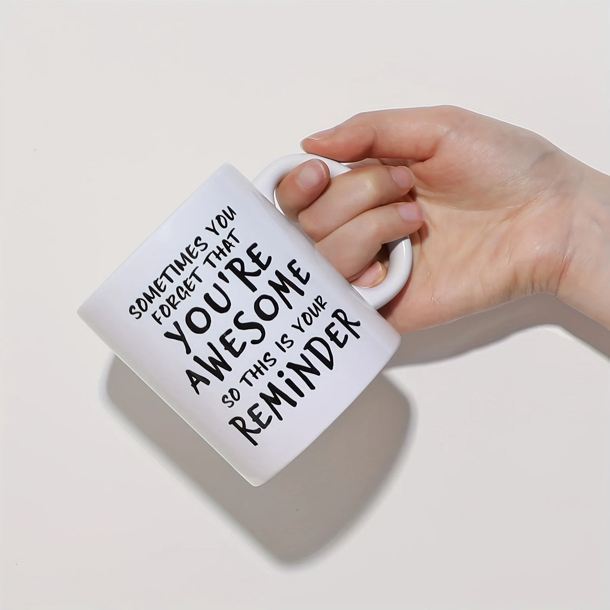 A hand is holding a white ceramic coffee mug with black text that reads Sometimes you forget that you're awesome so this is y