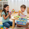A young girl and boy are playing with colorful squishy dumpling toys on a wooden table.