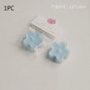 A single light blue flower-shaped soy wax tea light candle is packaged in clear plastic and displayed on a white background.