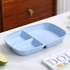 A light blue 3-compartment portion control plate is displayed on a white surface next to a lime and a book.