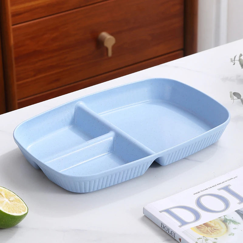A light blue 3-compartment portion control plate is displayed on a white surface next to a lime and a book.