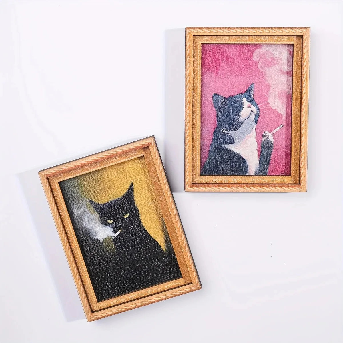 A framed watercolor painting of a black and white cat smoking, displayed next to a smaller framed painting.