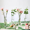 A set of twelve clear glass cylinder vases with pink and green floral arrangements on a white surface.