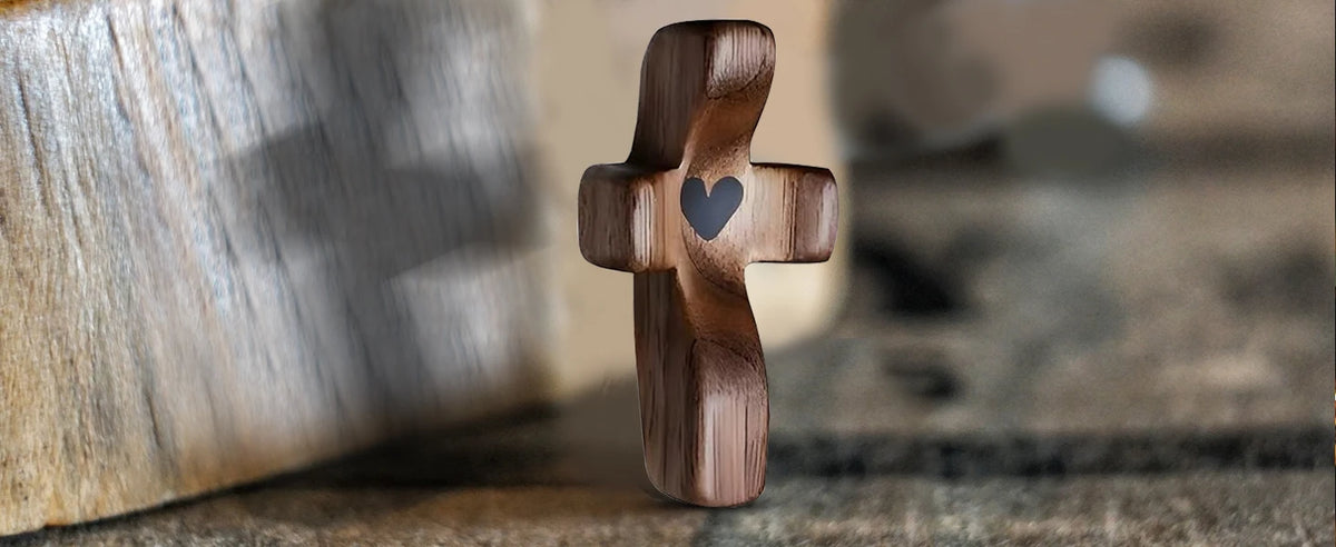 A dark wooden comfort prayer cross with a small heart carved into the center, resting on a textured surface.