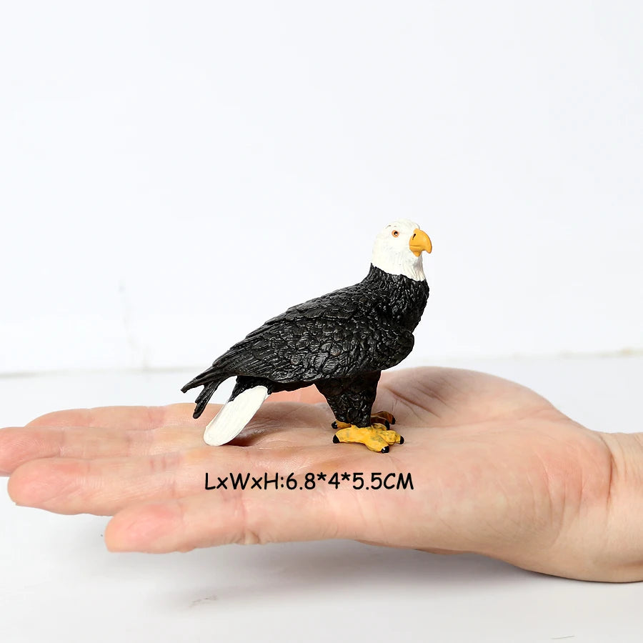 A realistic figurine of a black and white bird of prey, likely an owl or vulture, resting on a human hand.
