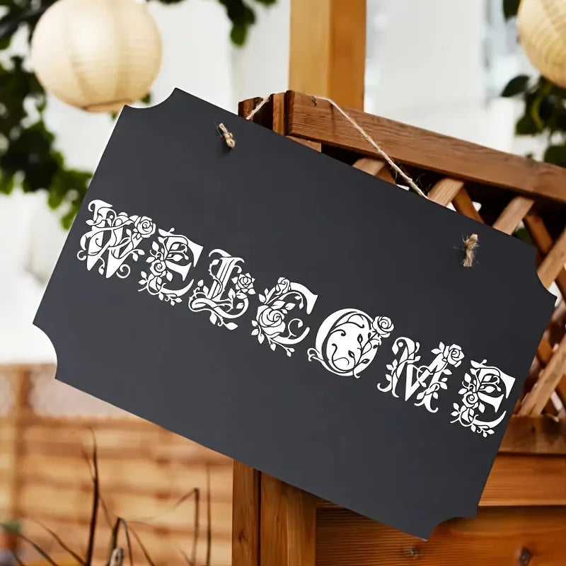 A black sign with white floral alphabet stencil letters spelling 'WELCOME' is displayed on a wooden tray.