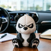 A cute angry panda figurine sitting on a wooden desk in front of a car dashboard.