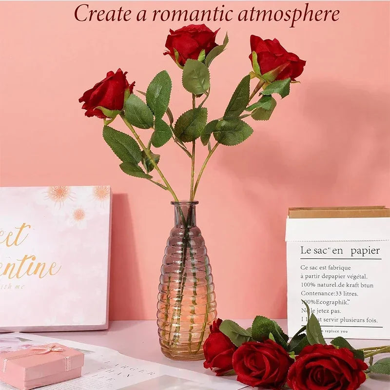 A bouquet of deep red artificial roses in a glass vase against a pink background.