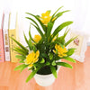 A vibrant artificial yellow lotus flower plant in a white pot displayed on a wooden surface next to books.