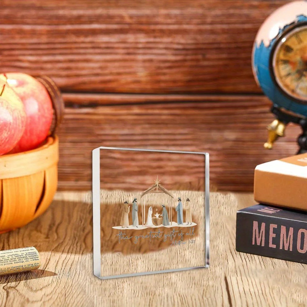 A clear acrylic nativity scene ornament featuring small figures set against a wooden background.