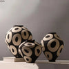A black and white ceramic vase with a geometric circle pattern is displayed on a white surface.