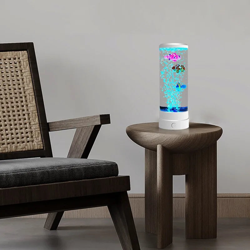 A tall, cylindrical LED lamp featuring a color-changing display of glowing fish, placed on a wooden table next to a dark chai