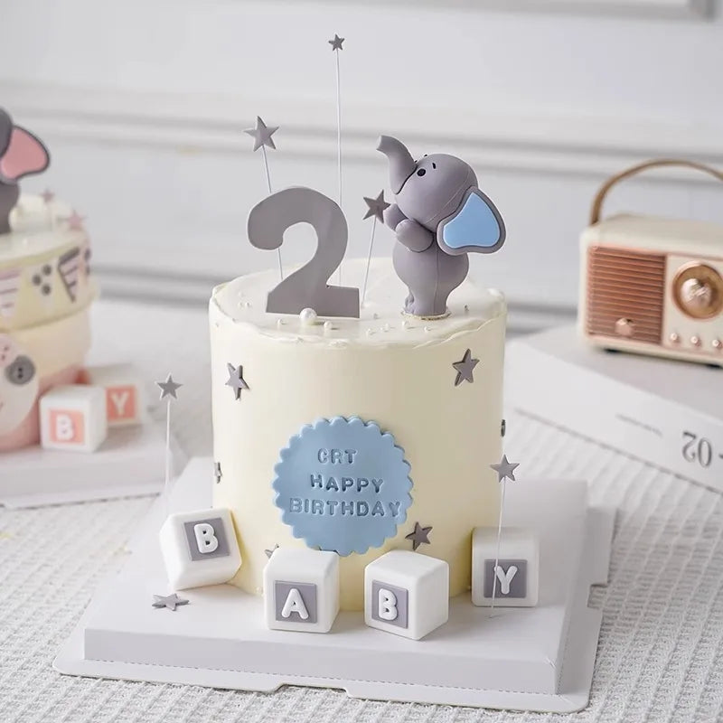 A cream-colored birthday cake decorated with a gray elephant topper and number 2 on a white stand.