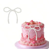 A pink tiered cake decorated with pink frosting and pearl bow accents, accompanied by a white pearl bow topper.