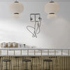 Elegant metal line art wall decor featuring a stylized figure and two large woven pendant lights above a bar area.